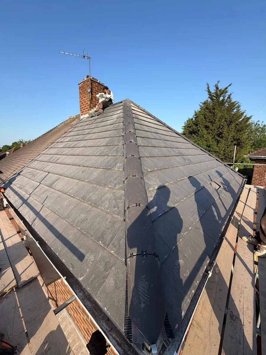 Grey hip roof with a brick chimney in bright sunlight