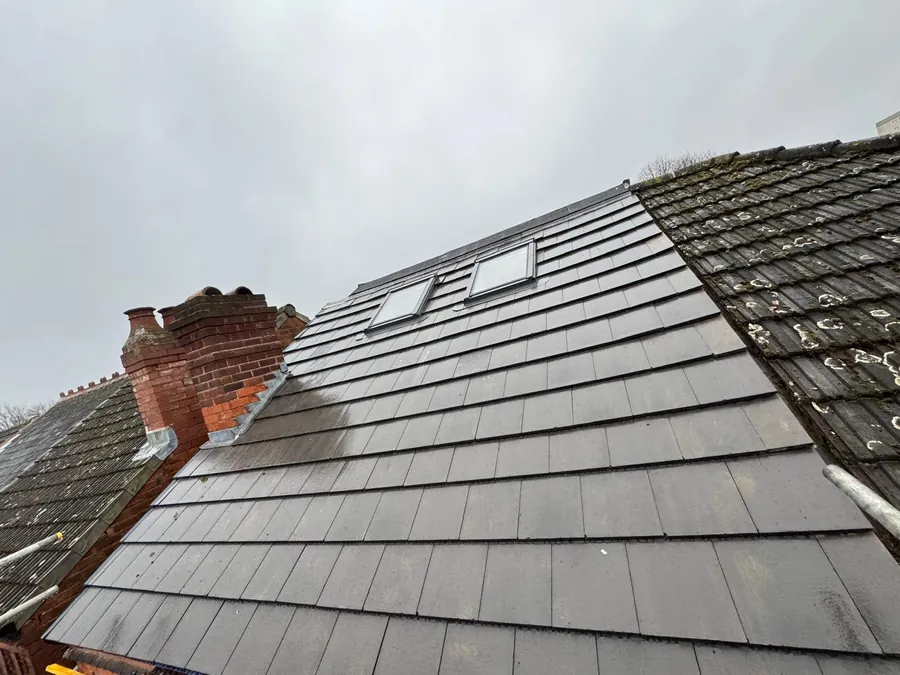 Grey slate-effect tiles around two rooflights beside a brick chimney