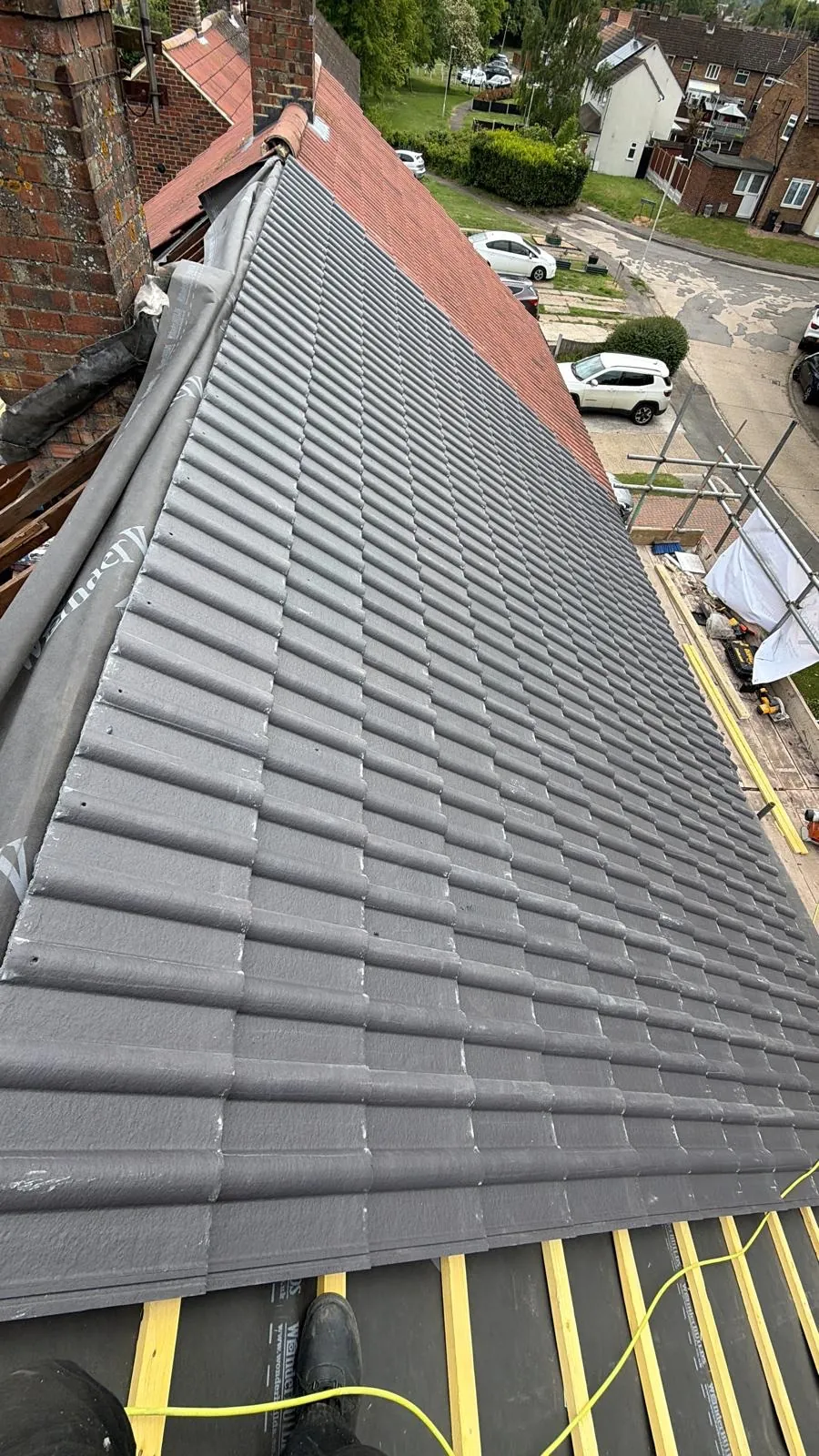 Grey interlocking tile courses being laid over yellow battens