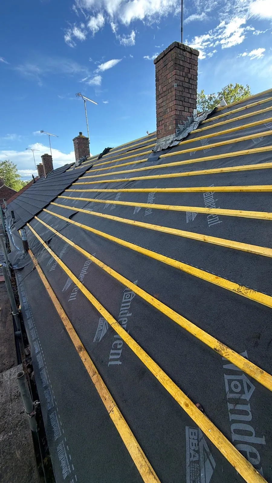 Yellow timber battens over dark membrane beside a brick chimney
